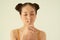 Keep in secret! Portrait of playful positive Asian teen girl with buns hairstyle showing silence gesture over light background