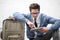 Keeping busy while he waits. A handsome young nerd sitting on the ground while typing on his tablet with luggage next to