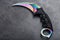 Kerambit dagger with a rainbow-colored blade on a dark textured background.