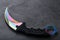 Kerambit dagger with a rainbow-colored blade on a dark textured background.