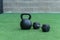 A Kettlebell and a hexagonal dumbbell side by side on synthetic grass