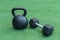 A Kettlebell and a hexagonal dumbbell side by side on synthetic grass