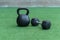 A Kettlebell and a hexagonal dumbbell side by side on synthetic grass