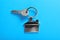Key with trinket in shape of house on blue background, top view. Real estate agent services