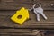 Key with yellow shaped house keychain on chain on wood texture background.