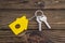 Key with yellow shaped house keychain on chain on wood texture background. Idea: