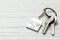 Keychain house and keys on white wooden background. Copy space for text.