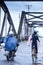 Khmer people riding motorcycles and bicycle across over the old French Bridge on rainy morning, Kampot, Cambodia