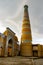 Khodja minaret and mosque madrasah in the historical center of Khiva with dark rain clouds, Uzbekistan