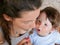 The kid asks to eat. Happy Smiling Caucasian Baby Boy makes a mess in a high chair and on his face while eating. watching mom eat