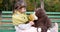 Kid on bench with yellow leaves in hands plays with teddy bear toy at playground in park