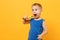 Kid boy 3-4 years old in blue shirt brush his teeth with toothbrush isolated on bright yellow orange wall background