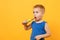 Kid boy 3-4 years old in blue shirt brush his teeth with toothbrush isolated on bright yellow orange wall background