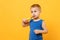 Kid boy 3-4 years old in blue shirt brush his teeth with toothbrush isolated on bright yellow orange wall background
