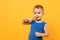 Kid boy 3-4 years old in blue shirt brush his teeth with toothbrush isolated on bright yellow orange wall background