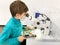 Kid boy conducts experiment with microscope in school lab. Curious inquisitive child learning physics and computer