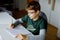 Kid boy with glasses learns at home for school. Preteen child making homework. Home schooling and distance learning