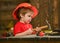 Kid boy hammering nail into wooden board. Child in helmet cute playing as builder or repairer, repairing or handcrafting