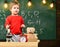 Kid boy near microscope in classroom, chalkboard on background. First former interested in studying, learning, education
