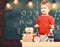 Kid boy near microscope in classroom, chalkboard on background. First former interested in studying, learning, education