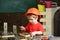 Kid boy in orange hard hat or helmet, study room background. Boy play as builder or repairer, work with tools. Child