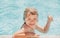 Kid boy swim in swimming pool with thumbs up. Happy little kid boy playing with in outdoor swimming pool on hot summer
