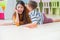 kid boy whisper teacher while lay down on library floor at kindergarten school.