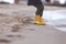 A kid in bright yellow rubber boots is playing at the surf zone of a sandy sea shore