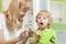 Kid brushing teeth near mirror in bathroom. His mother monitoring accuracy and time of cleaning action with hourglass.