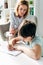 Kid with dyslexia drawing on paper with pencil and child psychologist looking at it