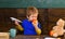 Kid eating apple with pleasure in class. Cute boy biting fruit with his eyes closed. Infant playing with paper plane