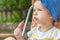 Kid eats red popsicles. Smiling Boy wears blue hat sitting in the yard with fruit ice cream outside in sunny day,Copy