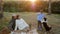 Kid feeds dog on rest with grandmother and grandfather on background of small river at sunset