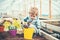 Kid filling yellow pot with soil, male hand holding hand fork. Blond kid playing in greenhouse. Educational game concept