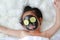 Kid girl in coal peeling face mask with cucumber, beauty concept