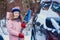 kid girl helping to clean car from snow on winter backyard or parking.