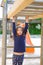 Kid girl playing in playground hanging from wood bars