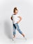 Kid girl preschooler in blue jeans and white t-shirt is dancing posing with foot behind showing dance moves on white
