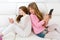 Kid girls having fun playing back to back with tablet pc on sofa