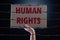 Kid hand holding cardboard paper with HUMAN RIGHTS text and rusty sharp bare wire on dark background, conceptual image