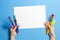 Kid hands with colorful paintbrushes and blank white paper sheet on blue background