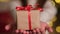 Kid hands giving small Christmas gift box on background of glowing lights