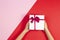 Kid hands holding present gift box with ribbon on red and pink background. Congratulations with Christmas, mother`s day