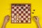Kid hands over a chessboard playing chess game on yellow background, top view