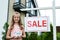 Kid holding carton house model near board with sale letters