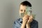 Kid holds euro banknotes in his hands near his face, looks with one eye, concept of pocket money, theft, shopping