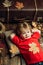 Kid lies laying his hands behind head and resting on wooden floor in golden leaves. Smiling little boy playing with