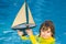 Kid play with toy sailing boat. Summer travel, kids holidays. Journey trip lifestyle yachting marine concept. Child