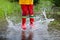 Kid playing out in the rain. Children with umbrella and rain boots play outdoors in heavy rain. Little boy jumping in muddy puddle