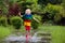 Kid playing out in the rain. Children with umbrella and rain boots play outdoors in heavy rain. Little boy jumping in muddy puddle